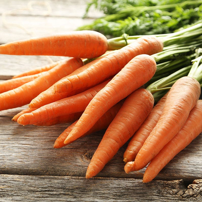 A bunch of freshly picked and rinsed hierloom carrots sit on a wooden tabletop